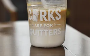 Detalle de vaso en U con texto 'CORKS ARE FOR QUITTERS' y bebida de café en varias capas