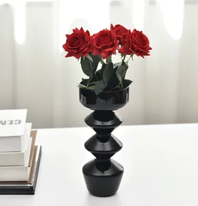 Dettaglio di un moderno vaso di vetro nero con rose rosse finte su scrivania bianca