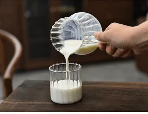Detailed shot of milk pouring from a ribbed glass pitcher into a matching cup