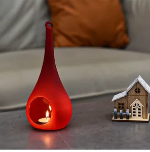 Close-up of red teardrop glass candle holder with lit tea light in a cozy setting