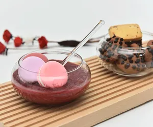 Detailed view of a handmade glass dessert bowl with a spoon on a wooden slatted board.