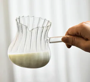 Close-up detail of a hand holding a striped heat-resistant glass milk pitcher with milk