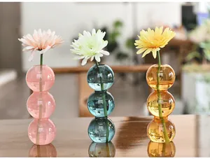 Detail view of colorful triple-bubble glass vases with daisies on a polished wooden surface