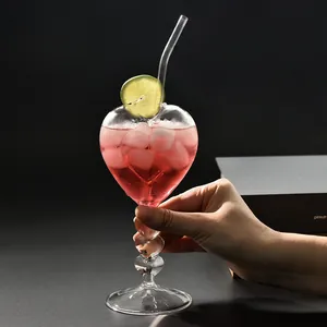 Creatief hartvormig cocktailglas met hoge voet vastgehouden met roze drankje en limoenschijfje