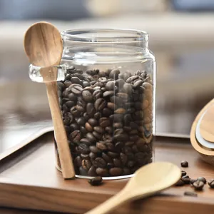 Glass coffee bean storage jar with airtight wooden lid and spoon on a tray
