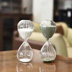 Relojes de arena nórdicos de vidrio con arena blanca y verde sobre mesa de madera