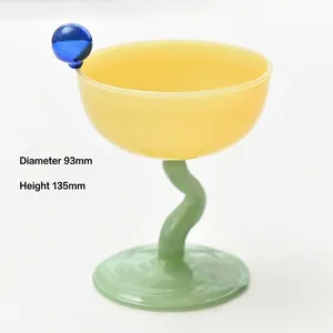 Primo piano di coppa da dessert in vetro giallo e verde con stelo ondulato e perla blu.