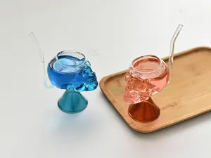 Detalle de copa de cristal con forma de calavera y pajita sobre bandeja de madera