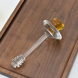 Nahaufnahme eines Honiglöffels aus Glas mit einem niedlichen bernsteinfarbenen Bären