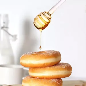 Nahaufnahme eines Honiglöffels aus Glas, der Sirup auf frische Zucker-Donuts tropft