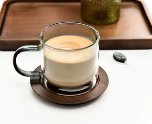Close-up detail of a double-walled glass coffee mug filled with latte on a wooden coaster