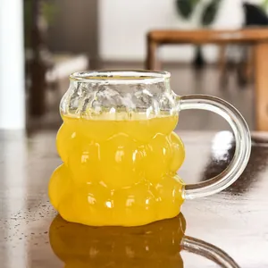 Macro view of textured grape-shaped glass mug with orange juice on wooden table