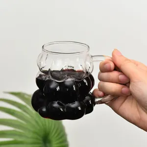 Hand holding a creative grape-shaped glass mug with dark purple juice and a handle
