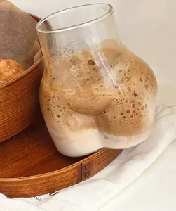Primer plano de un creativo vaso de cristal con forma de trasero y café espumoso en bandeja.