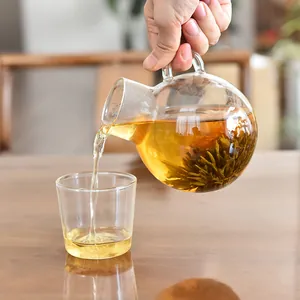Close-up of a clear glass teapot pouring blooming flower tea into a matching cup