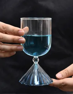 Elegante copa de postre de vidrio con base acanalada y líquido azul sostenida por manos.