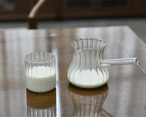 Close-up of heat-resistant striped glass milk pitcher with handle and matching cup on wood.
