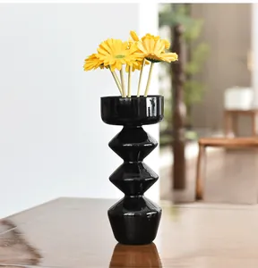 Vaso moderno in vetro nero geometrico con fiori gialli su un tavolo lucido in legno