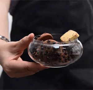 Hand holding a clear round glass dessert bowl filled with chocolate chip cookies