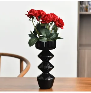 Moderno vaso in vetro nero a forma di bolla con rose rosse su un tavolo in legno