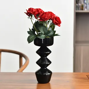 Vaso artistico moderno in vetro nero con rose rosse su un tavolo di legno rustico