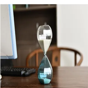 Modern glass hourglass sand timer with blue tint on an office desk for productivity