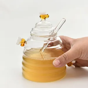 Close-up of a clear beehive glass honey jar with a glass dipper and cute bee accents