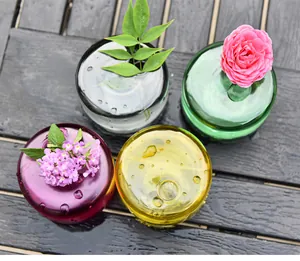 Draufsicht auf vier farbenfrohe Mini-Glasvasen mit Blumen auf dunklem Holz im Detail