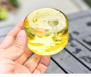 Nahaufnahme einer Hand, die eine kleine gelbe Glasvase mit Luftblasendetails hält