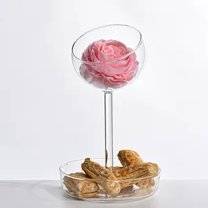 Vista laterale del servitore in vetro con fiore rosa nella ciotola e pasticcini sul vassoio