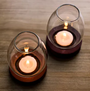 Top view of two clear glass candle holders with warm lit tea lights on wooden base