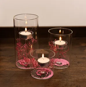 Detailopname van drie glazen windlichten met brandende theelichtjes en roze bloemen