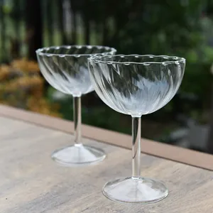Ribbed glass champagne coupes with scalloped rim shown in a set of two on wooden table