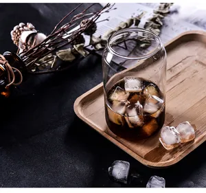 Atmospheric detail shot of can-shaped glass cup with iced coffee on wooden tray
