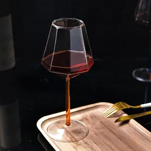Elegantes geometrisches Kristall-Weinglas mit bernsteinfarbenem Stiel auf einem Holztablett