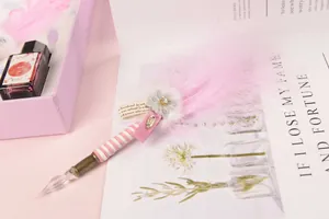 Elegant pink feather glass dip pen set with red ink bottle on a magazine background