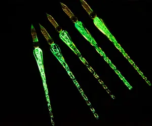 Detailed close-up of luminous green glass dip pens glowing in the dark