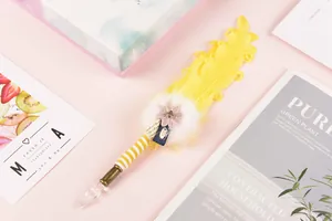 Close-up of a handmade yellow feather glass dip pen with a decorative pink flower.