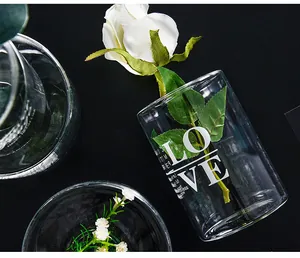 Close-up of clear glass vase with white 'LOVE' lettering and artificial rose