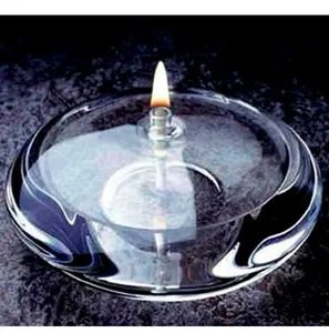Close-up of a modern clear glass oil lamp with a lit wick on a dark textured surface.