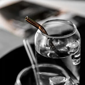 A creative clear rounded glass cup featuring a curved amber glass straw for cold drinks.