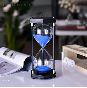 Gedetailleerd beeld van een moderne zandloper met blauw zand en zwart frame op bureau.