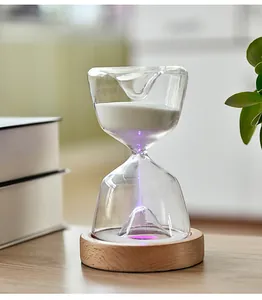 Detail view of a glowing glass hourglass timer with purple LED light on wooden base