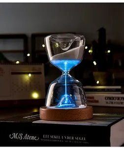 Beautiful luminous glass hourglass night light with glowing blue sand on a wooden base.