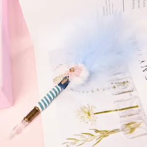 Handmade glass dip pen with light blue feather and striped handle on artistic background