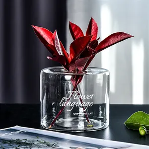 Minimalist glass vase with letter print and vibrant red leaves in lifestyle setting