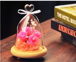 Detailed view of a heart-topped glass dome with pink preserved roses on a wooden base