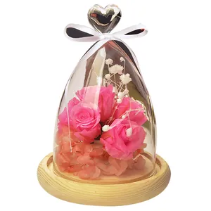 Elegant heart-top glass dome gift featuring pink preserved roses on a natural wooden base