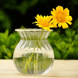 Primer plano de un jarrón de cristal transparente con forma de oliva y flores amarillas