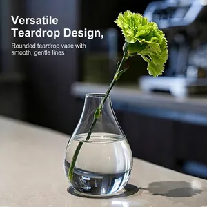 Vaso minimalista in vetro trasparente a goccia con un garofano verde sul piano